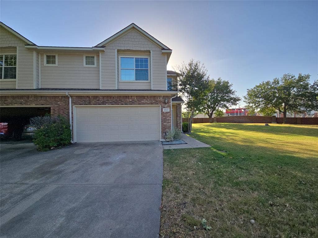 8621 Brunswick Drive, Plano, TX 75024 Brick and siding exterior with an attached garage, concrete driveway, and a spacious grassy area with mature trees