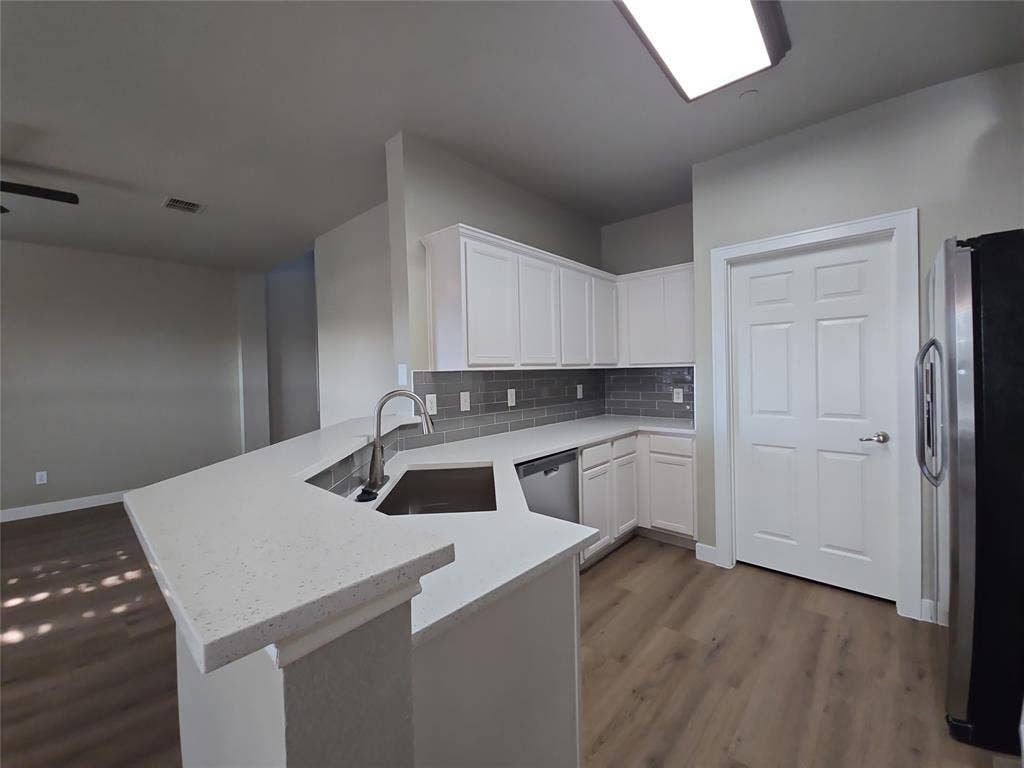 8621 Brunswick Drive, Plano, TX 75024 White cabinetry, solid surface countertops, stainless steel appliances, subway tile backsplash, and wood-finish flooring