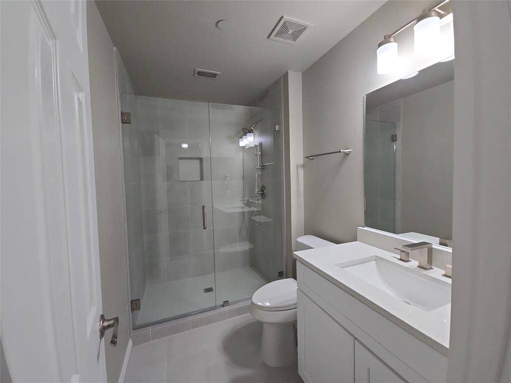 8621 Brunswick Drive, Plano, TX 75024 Glass-enclosed shower with a recessed shelf, white vanity with an integrated sink, brushed nickel faucet, and a wall-mounted mirror