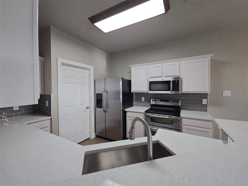 8621 Brunswick Drive, Plano, TX 75024 White cabinetry, stainless steel appliances, grey subway tile backsplash, white countertops, and an undermount sink with a gooseneck faucet