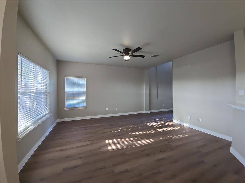 8621 Brunswick Drive, Plano, TX 75024 Spacious room featuring wood-finish flooring, multiple windows with blinds, a ceiling fan with integrated lighting, and neutral wall tones