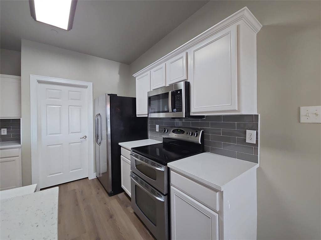 8621 Brunswick Drive, Plano, TX 75024 White shaker-style cabinetry with crown molding, stainless steel appliances, wood-finish flooring, white countertops, and a gray subway tile backsplash