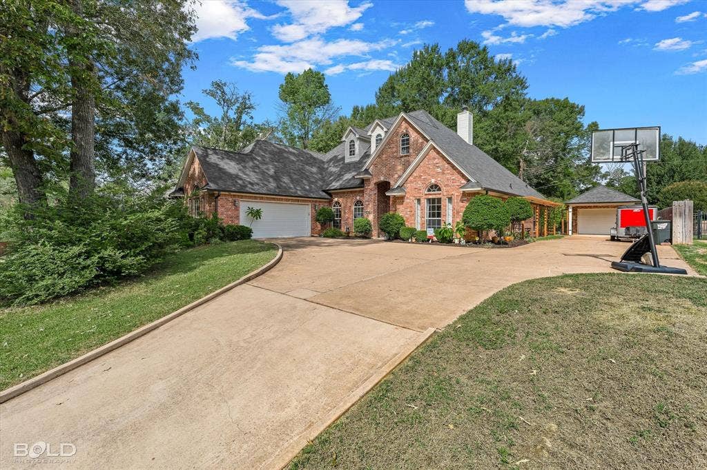 206 Silver Fox Circle, Haughton, LA 71037 Multi-gabled brick exterior featuring a multi-car garage, expansive concrete driveway, arched windows, and a detached structure