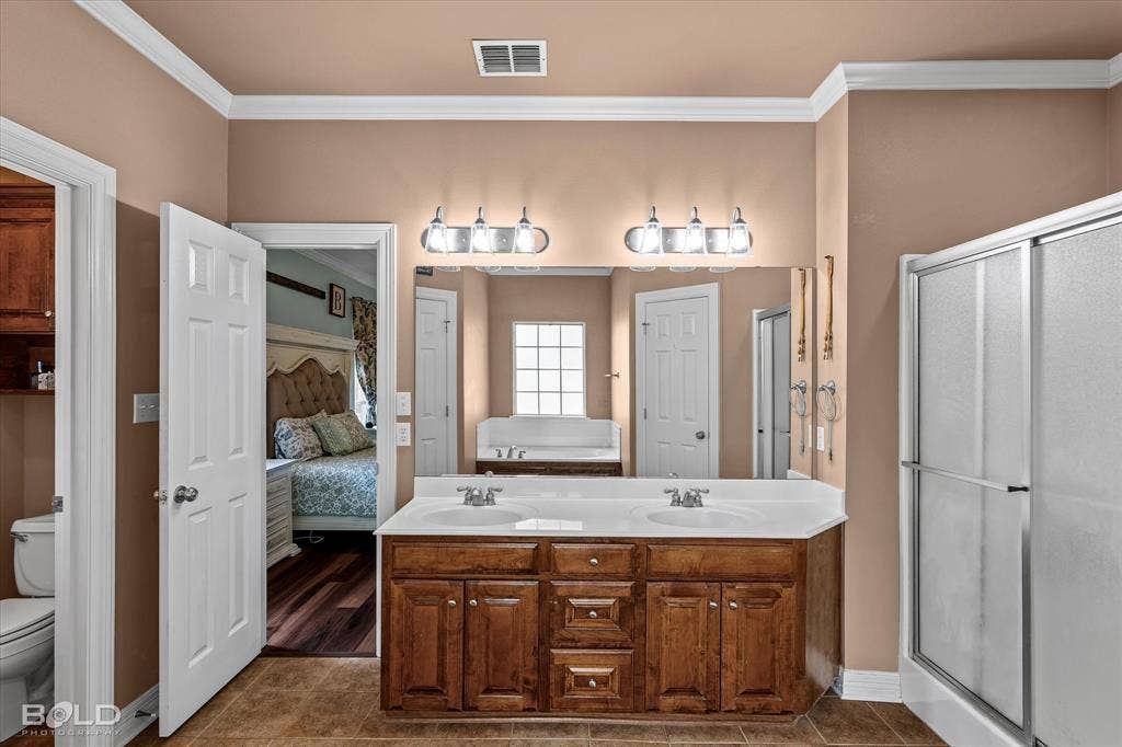 206 Silver Fox Circle, Haughton, LA 71037 Double vanity featuring wood-finish cabinetry, a white countertop with integrated dual sinks, two multi-light wall fixtures, and a large plate-glass mirror