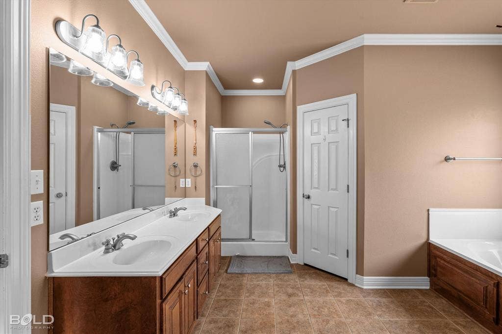 206 Silver Fox Circle, Haughton, LA 71037 Dual-sink vanity with a solid-surface countertop, full-width mirror, crown molding, glass-enclosed shower, and a built-in soaking tub with wood-finish cabinetry