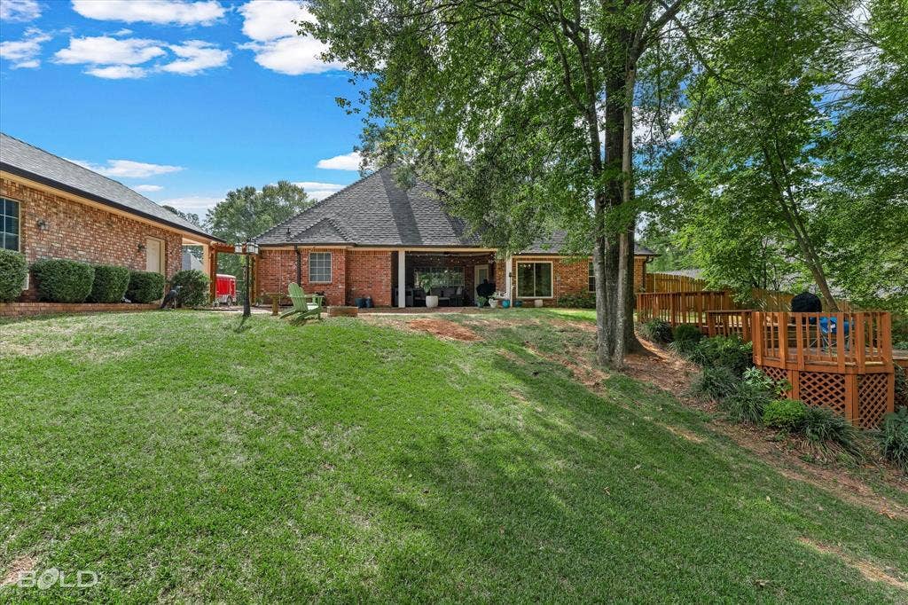 206 Silver Fox Circle, Haughton, LA 71037 Brick exterior featuring a covered patio, tiered wood deck with lattice skirting, and mature trees on a grass lawn