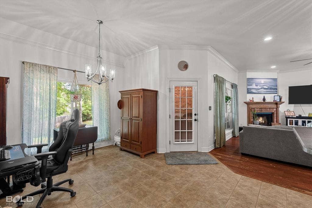 206 Silver Fox Circle, Haughton, LA 71037 Multi-functional space featuring tile flooring, crown molding, a decorative chandelier, a glass-paneled exterior door, and a fireplace with a wood mantel