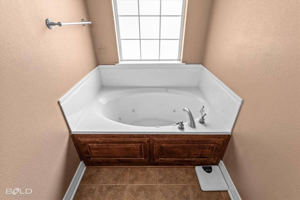 206 Silver Fox Circle, Haughton, LA 71037 Jetted soaking tub with a white surround, custom wood-paneled apron front, brushed nickel deck-mounted faucet, and windowed alcove featuring tile flooring