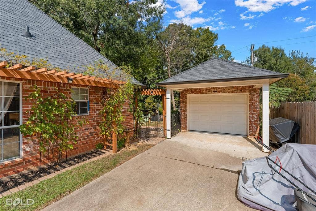 206 Silver Fox Circle, Haughton, LA 71037 Exterior brick facade with a wooden pergola, detached garage featuring a shingled roof, and a gated side entrance