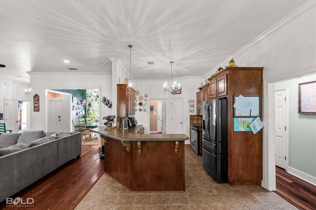 206 Silver Fox Circle, Haughton, LA 71037 Kitchen featuring stained wood cabinetry, raised breakfast bar with stone-finish countertop, tile flooring, and multi-light chandelier fixture