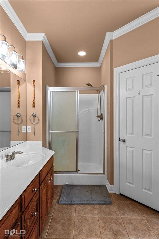 206 Silver Fox Circle, Haughton, LA 71037 Bathroom featuring crown molding, ceramic tile flooring, a wood-finish vanity with a composite countertop, a framed wall mirror, and a walk-in shower with a sliding glass enclosure