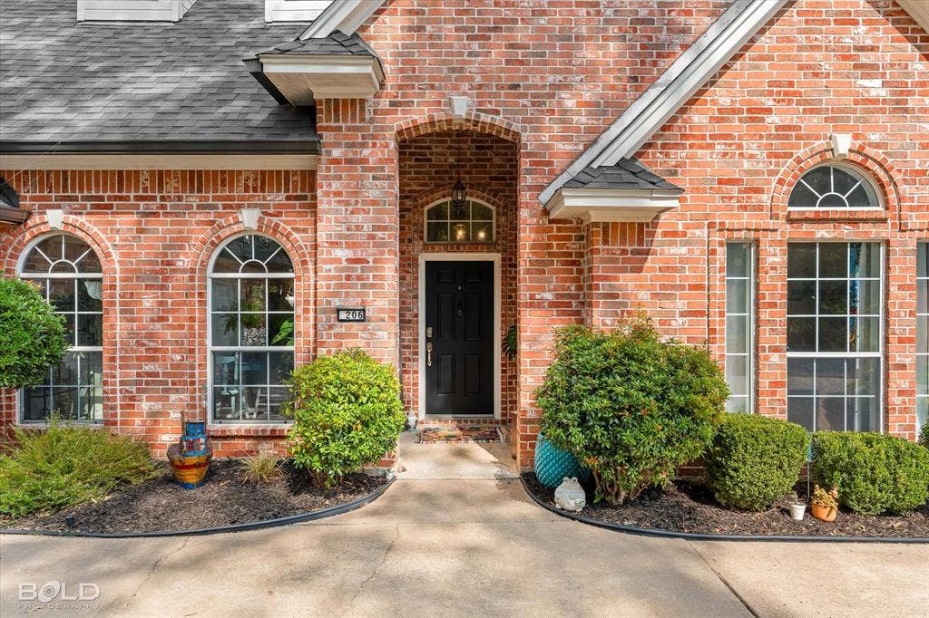 206 Silver Fox Circle, Haughton, LA 71037 Red brick exterior facade featuring an arched entryway, shingle roofing, and multi-light windows with arched transoms