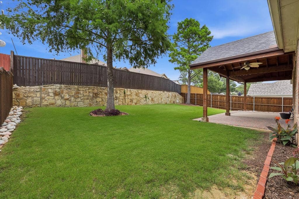 Expansive backyard with a manicured lawn, stone retaining wall, and a wood-slat privacy fence