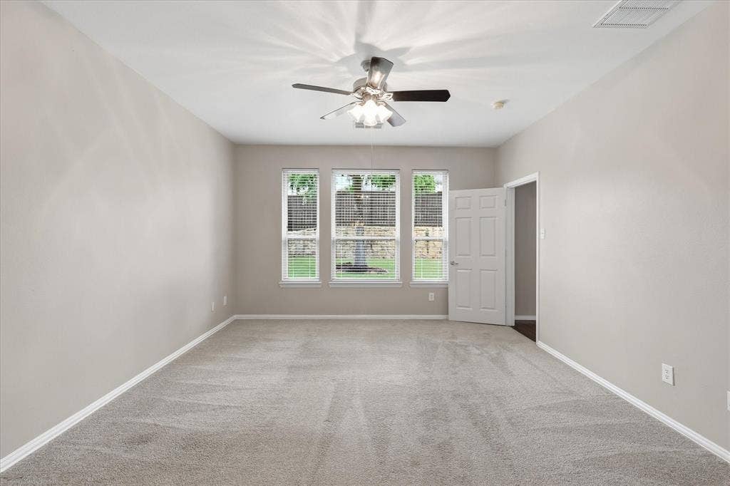 Spacious room featuring neutral carpeting, a ceiling fan with integrated lighting, and three large windows