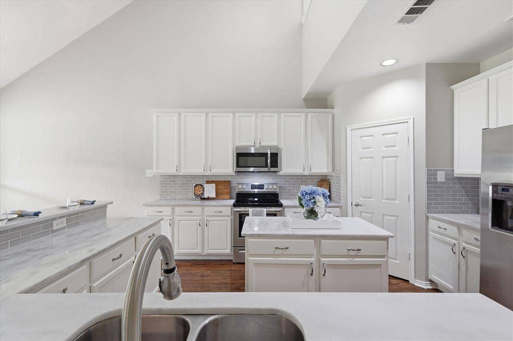 Kitchen featuring white cabinetry, light-colored countertops, stainless steel appliances, a center island, and a tile backsplash