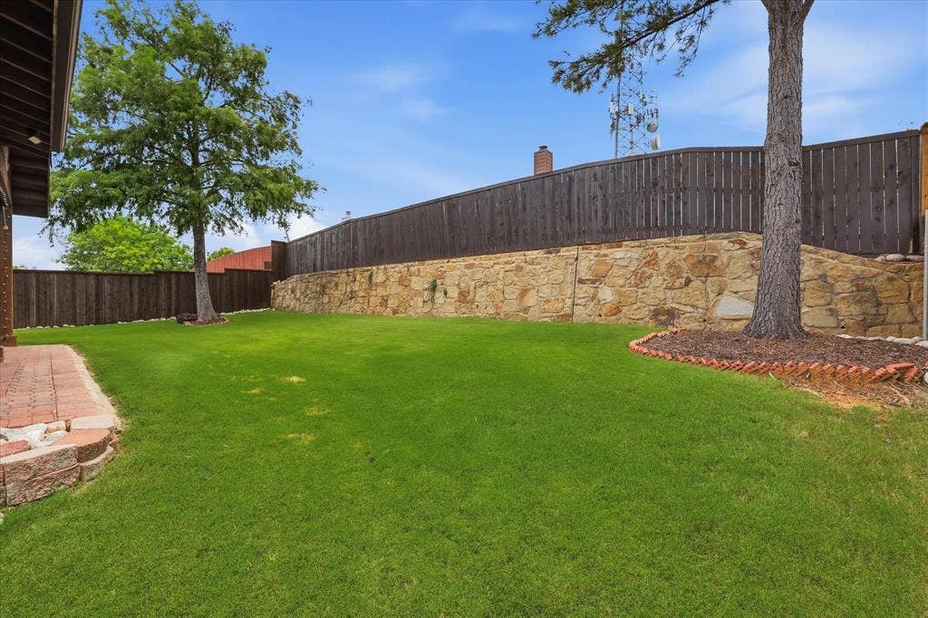Expansive lawn area with a stone retaining wall, mature trees, and a privacy fence