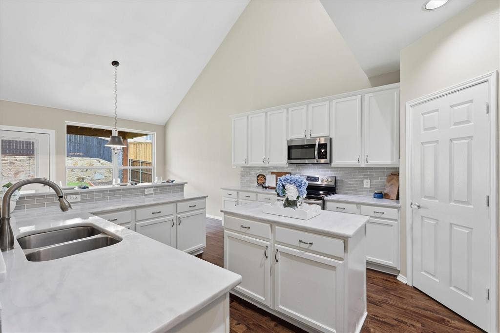 Vaulted ceiling with recessed lighting, white cabinetry, stainless steel appliances, stone-finish countertops, and wood-finish flooring