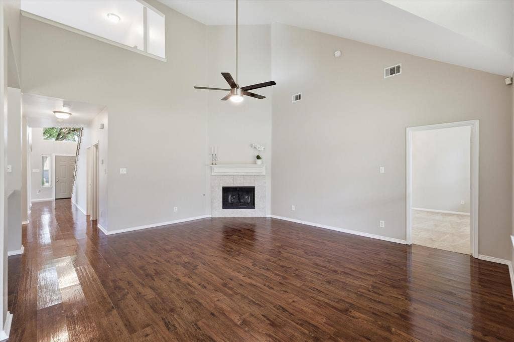 Spacious living area with high vaulted ceilings, wood-finish flooring, and a corner fireplace featuring a decorative mantle