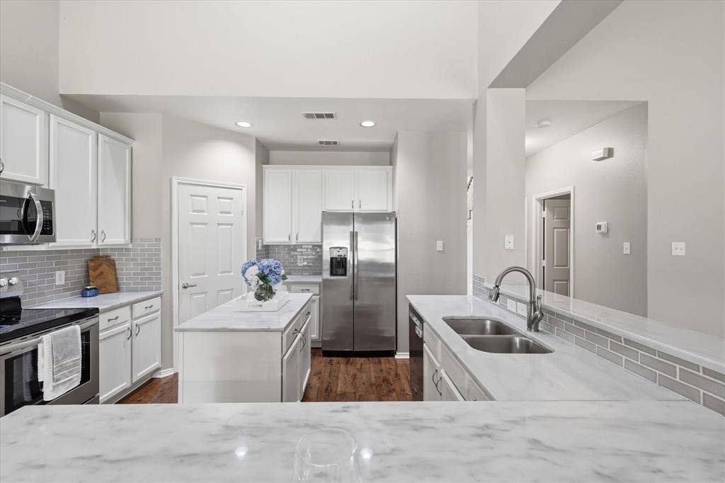 Kitchen featuring white cabinetry, stainless steel appliances, a center island, light-toned countertops, and a gray subway tile backsplash