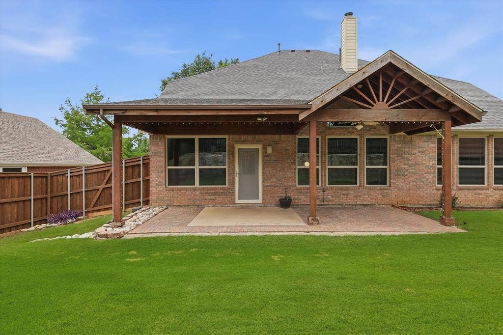 Expansive backyard featuring a covered patio with a vaulted ceiling, brick exterior, and a wood privacy fence