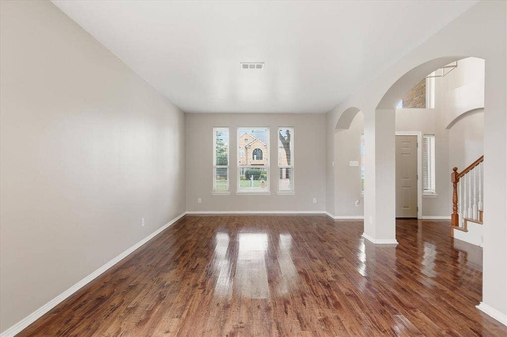Expansive interior with wood-finish flooring, multiple arched doorways, and a staircase with a wooden handrail