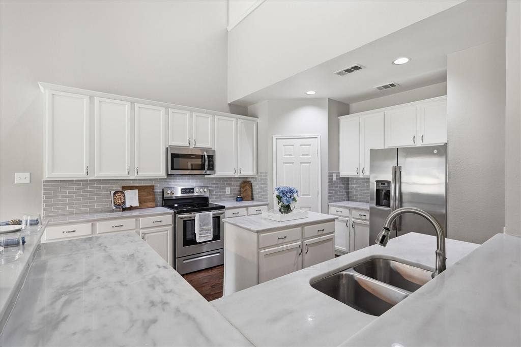 Kitchen featuring a large island, stainless steel appliances, white cabinetry, undermount double-basin sink, and a tile backsplash