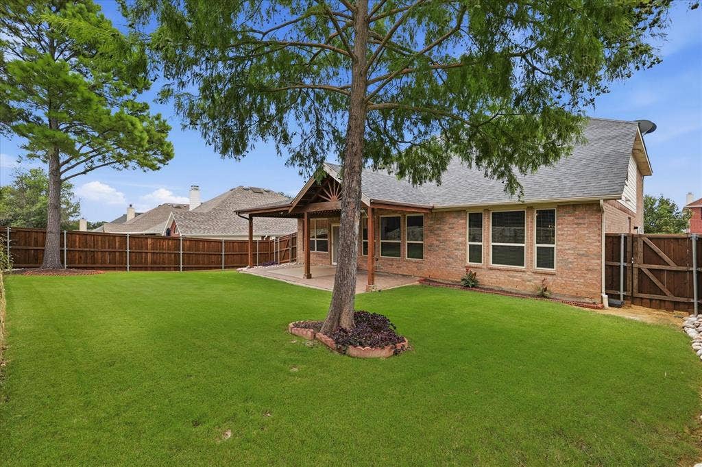 Expansive lawn with a full privacy fence, brick exterior, and covered patio featuring a wood-beam ceiling