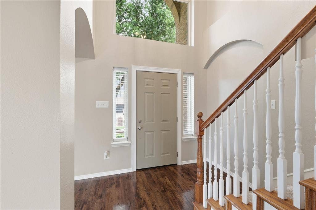 Entryway featuring wood-finish flooring, a two-story ceiling, arched architectural details, and a staircase with a wood handrail and white balusters