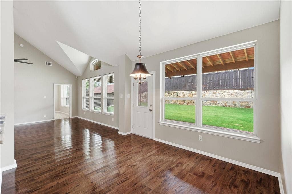 Vaulted ceiling, wood-finish flooring, multiple windows, built-in chandelier, and a white door with an integrated window