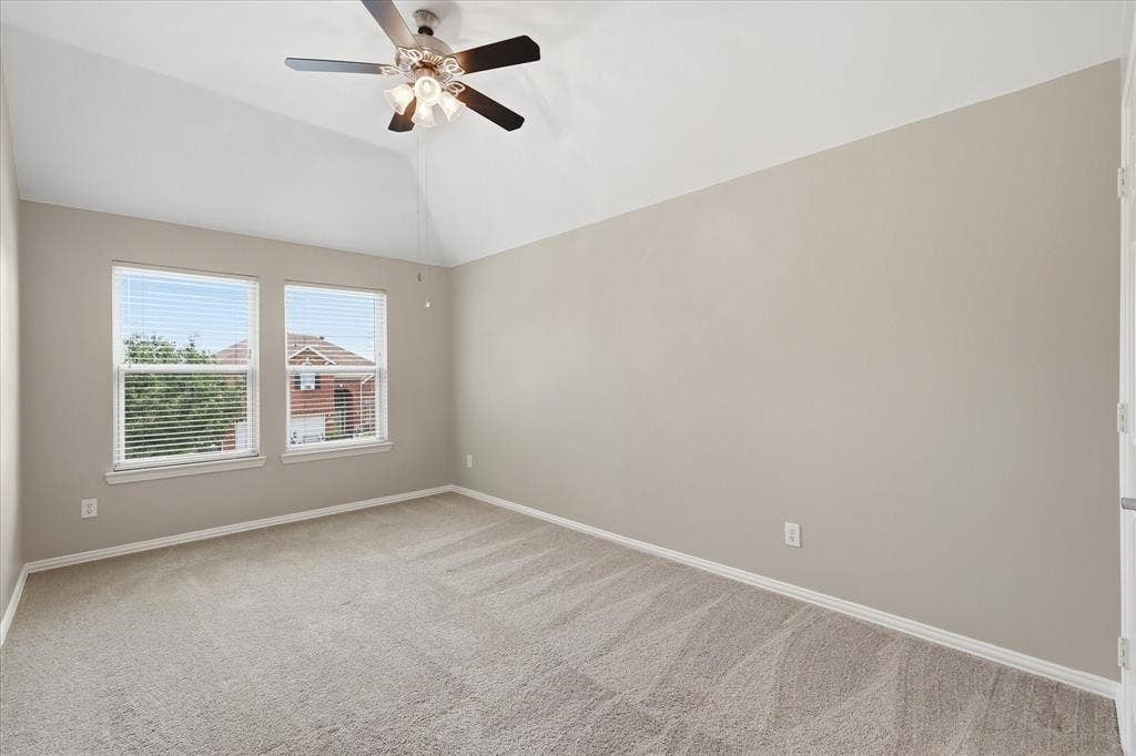 Vaulted ceiling with a ceiling fan, two windows with blinds, neutral-toned walls, and carpeted flooring