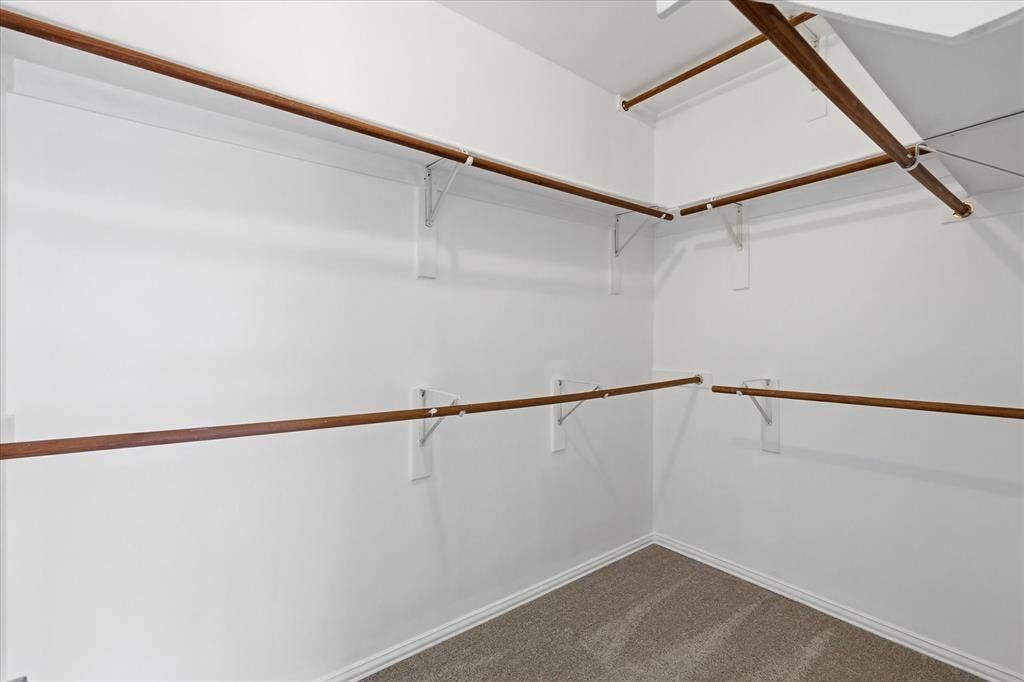 Customizable closet system with multiple wood-finish rods, white shelving supports, and neutral carpeting