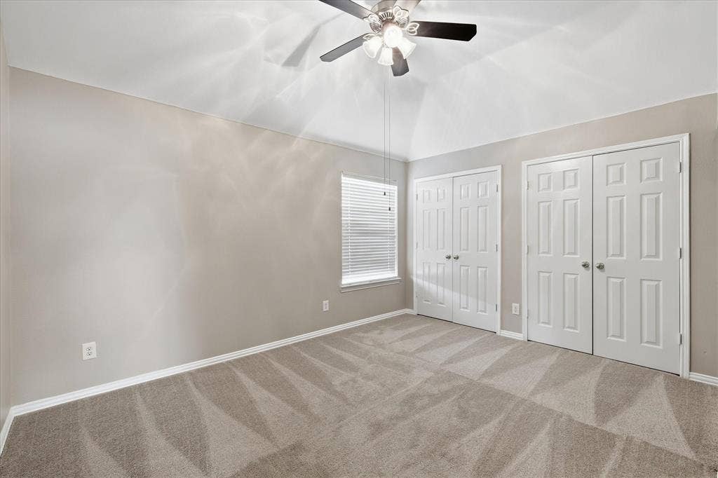 Vaulted ceiling with a ceiling fan, two closet systems with bifold doors, window with horizontal blinds, and neutral carpet flooring