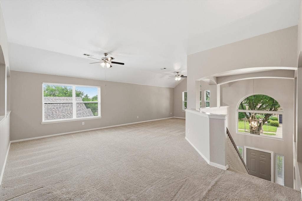 Spacious carpeted area featuring vaulted ceilings, multiple windows, and ceiling fans