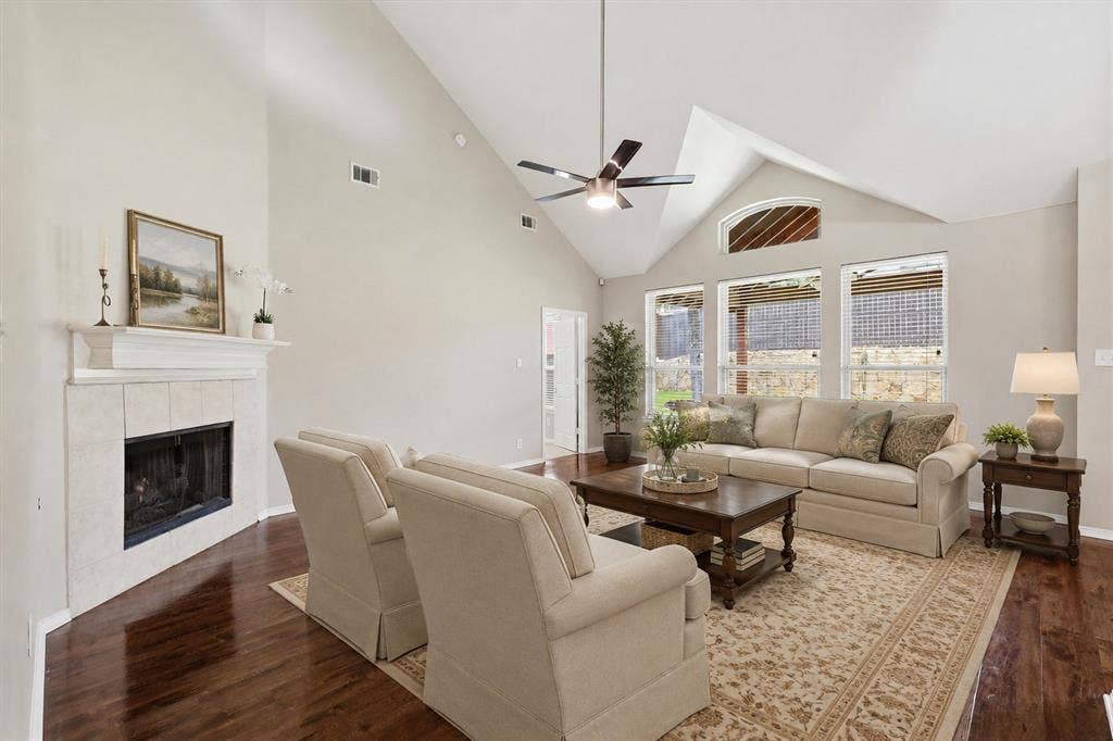 Vaulted ceiling with an attached ceiling fan, hardwood-finish flooring, and a tiled fireplace