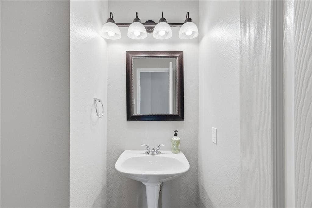 Pedestal sink with chrome faucet, framed mirror, and a four-light vanity fixture