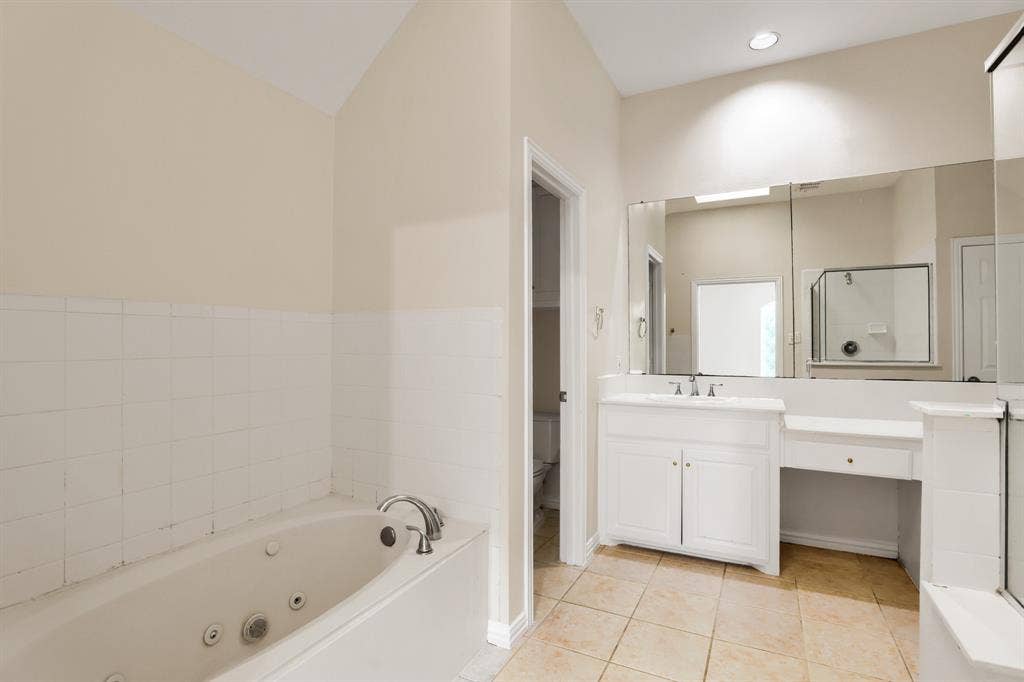 8115 Dogwood Lane, Irving, TX 75063 Jetted soaking tub, white tile wainscoting, white vanity with integrated sink, extensive wall-mounted mirror, and tiled flooring
