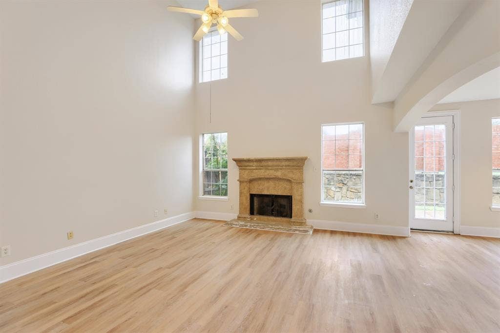 8115 Dogwood Lane, Irving, TX 75063 Two-story living space featuring a fireplace with stone surround, wood-finish flooring, high ceilings, and multiple windows