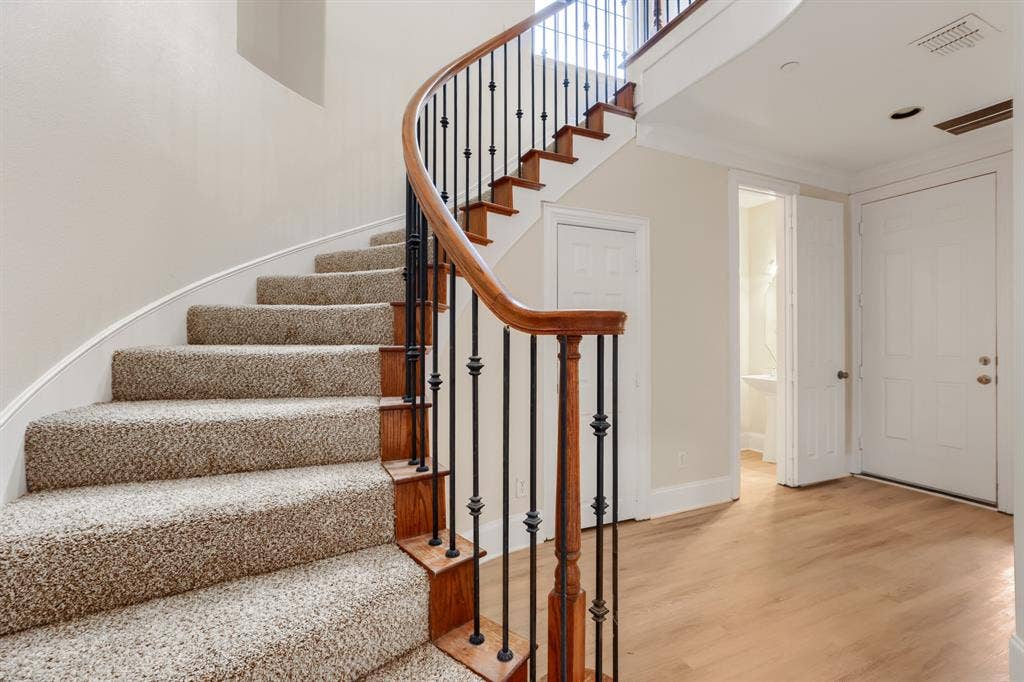 8115 Dogwood Lane, Irving, TX 75063 Curved staircase with wood railing, wrought iron balusters, and carpeted treads