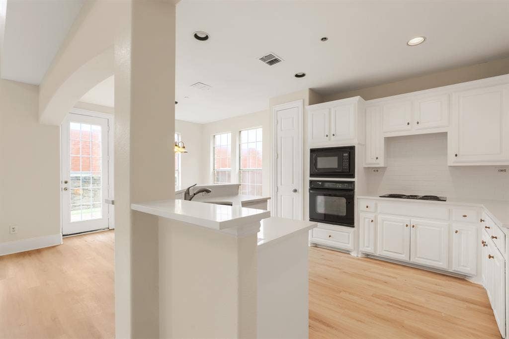 8115 Dogwood Lane, Irving, TX 75063 Kitchen featuring white cabinetry, built-in double ovens, a built-in microwave, white countertops, and wood-finish flooring
