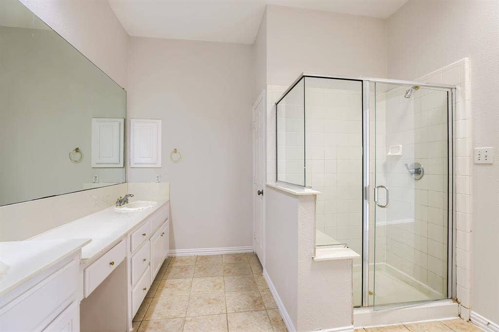 8115 Dogwood Lane, Irving, TX 75063 Extended vanity with integrated sink, full-width mirror, tile flooring, and a glass-enclosed shower