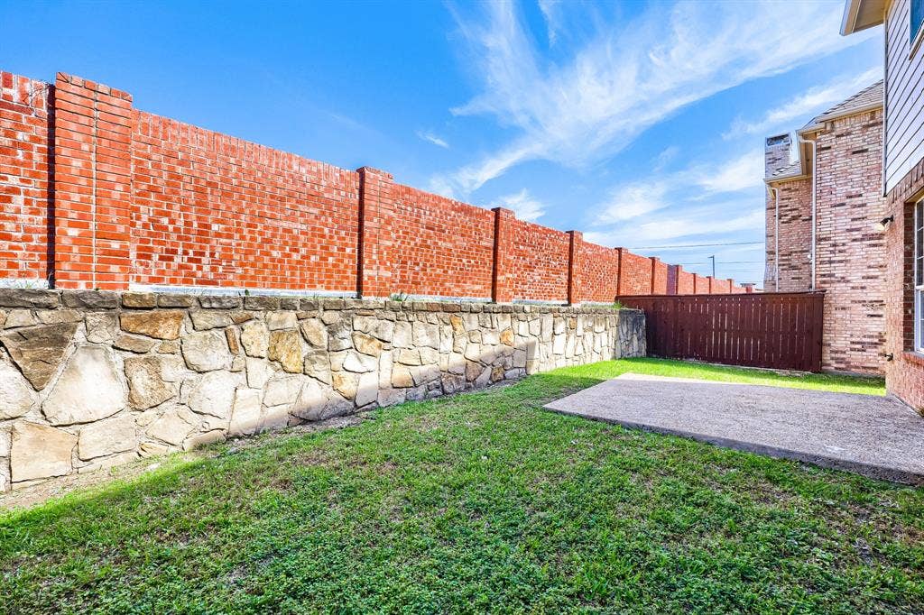 8115 Dogwood Lane, Irving, TX 75063 Private backyard featuring a concrete patio, a stone and brick privacy wall, and a wood privacy fence