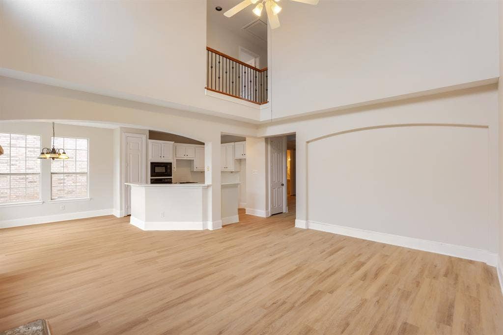 8115 Dogwood Lane, Irving, TX 75063 Vaulted ceiling, wood-finish flooring, white cabinetry, built-in microwave, and an interior balcony with wood and wrought iron railing