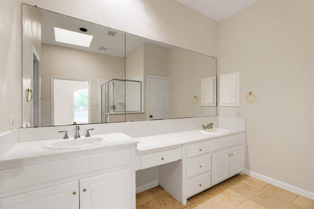 8115 Dogwood Lane, Irving, TX 75063 Dual vanity sinks with white cabinetry, a built-in vanity area, and a skylight