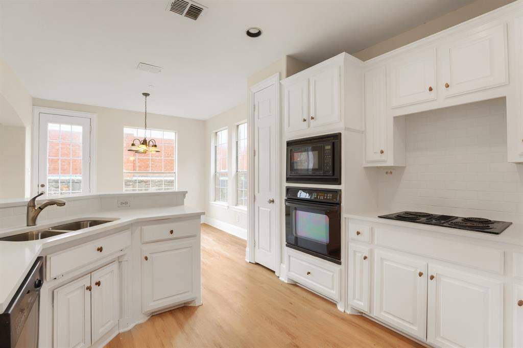 8115 Dogwood Lane, Irving, TX 75063 Kitchen featuring light wood-finish flooring, white cabinetry with brass-toned hardware, double basin sink with a gooseneck faucet, built-in microwave, and an electric cooktop