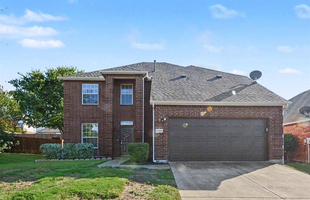 6509 Cartier Court, McKinney, TX 75072 Brick exterior facade, dark shingle roof, attached garage with panel door, concrete driveway, and established front landscaping