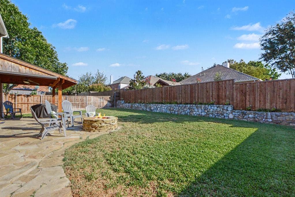 6509 Cartier Court, McKinney, TX 75072 Expansive backyard featuring a stone patio, wooden pergola, built-in stone fire pit, and wood privacy fencing with a stacked stone retaining wall