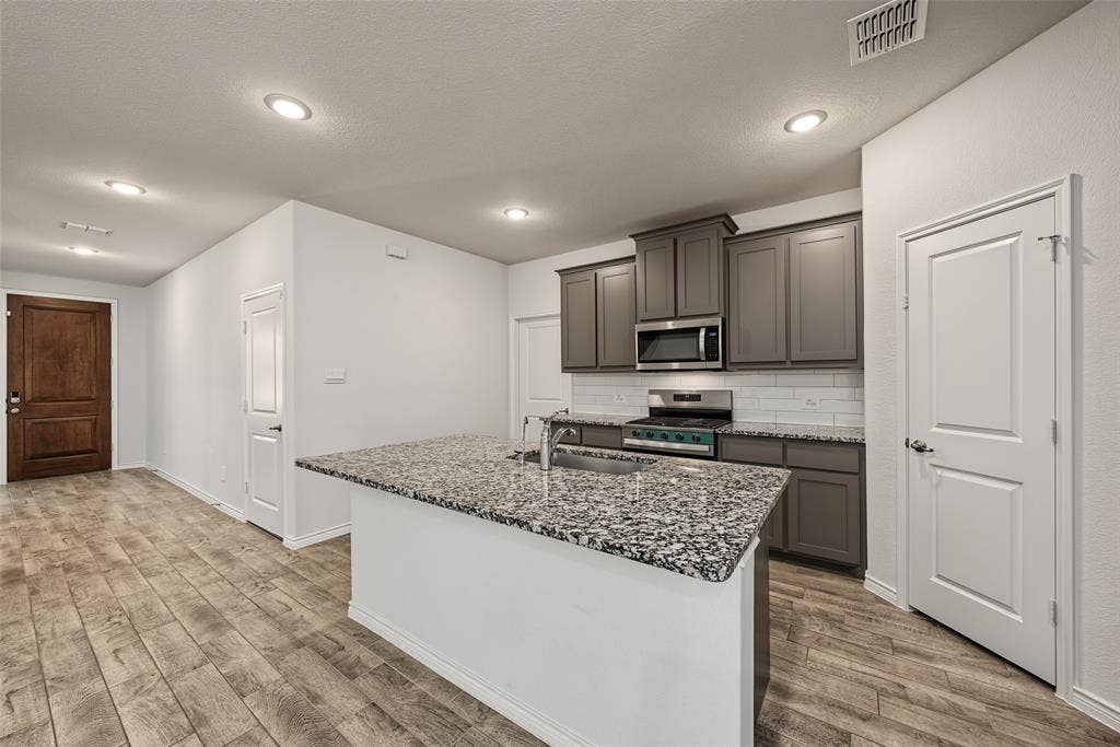 Kitchen featuring gray cabinetry, stainless steel appliances, a white subway tile backsplash, and a large island with a speckled granite countertop