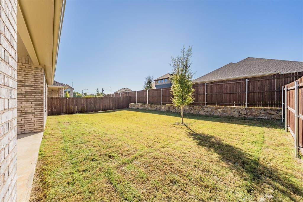 Expansive backyard featuring a manicured lawn, established tree, and a natural stone retaining wall