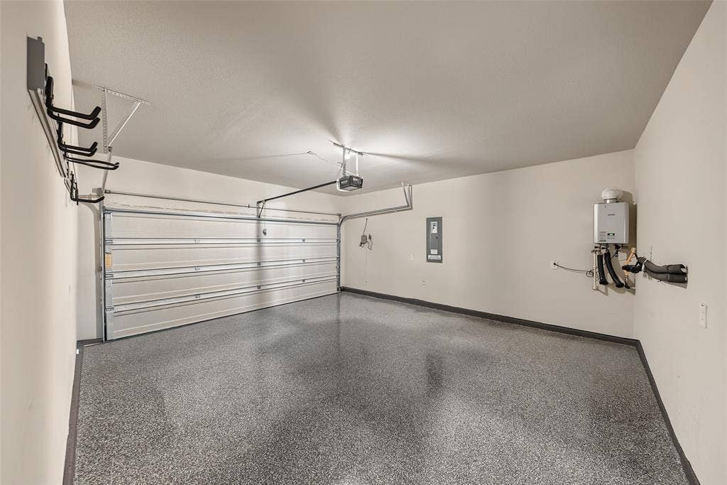 Garage with speckled epoxy flooring, overhead door opener, wall-mounted storage racks, and a tankless water heater