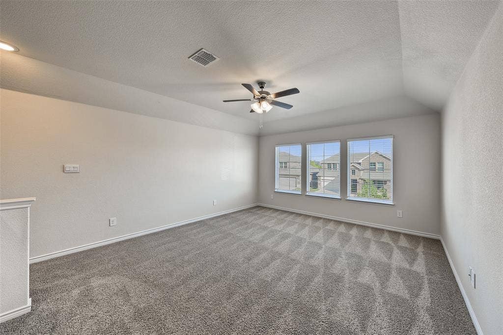 Spacious room featuring vaulted ceilings, a ceiling fan with integrated lighting, three windows with horizontal blinds, and carpet flooring